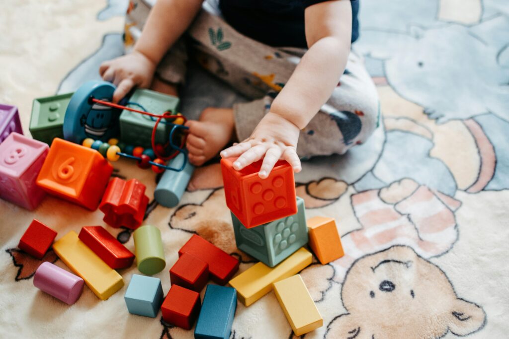 pexels photo 5435599 5435599 Toddler engaging with vibrant toy blocks on a patterned rug in a playful setting.